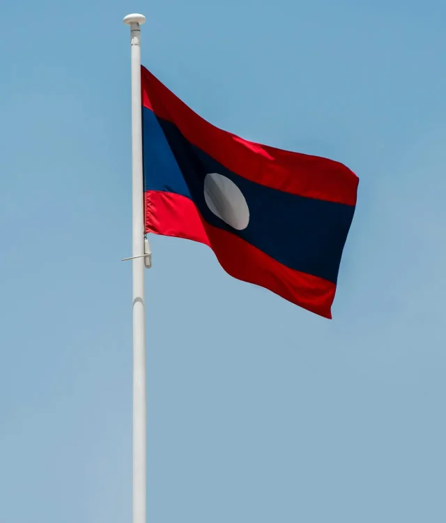Vertical shot of the Lao national flag waving against a clear blue sky in Vientiane.