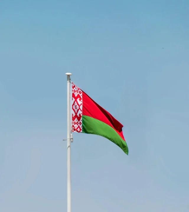 pexels-photo-13992197-13992197 Belarus national flag waving on a flagpole against a clear blue sky, showcasing patriotism.