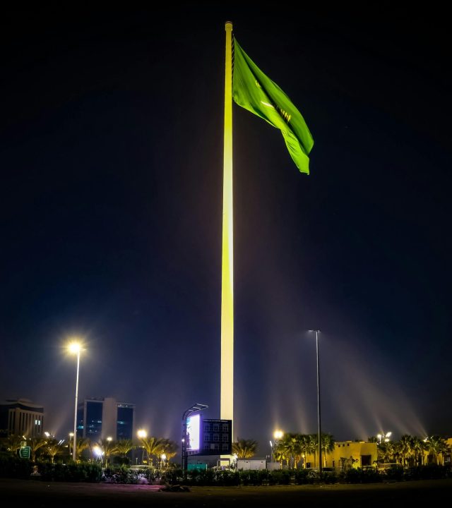 Majestic Saudi Arabian flag illuminated against the night sky, surrounded by cityscape lights in Riyadh.