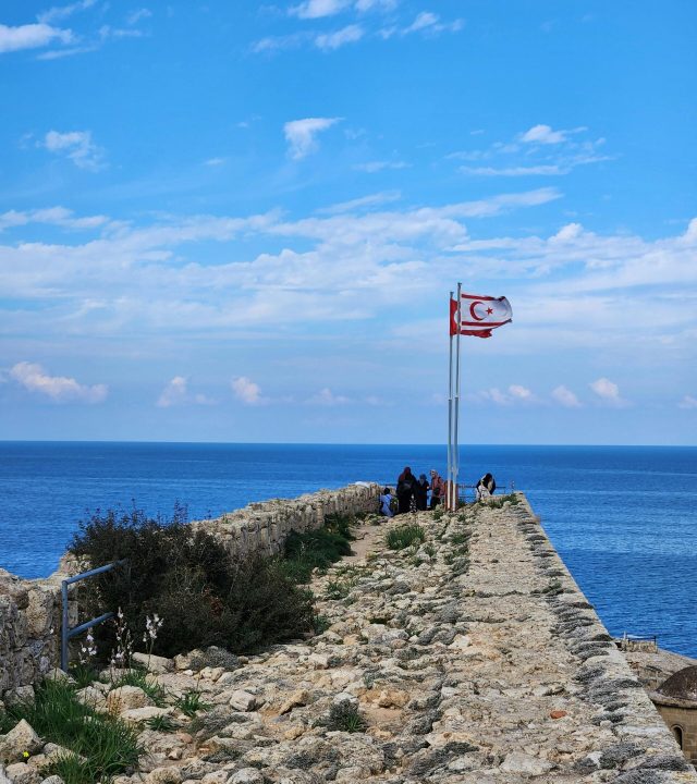 Historic Kyrenia Castle with flags overlooking the sea on a bright day.